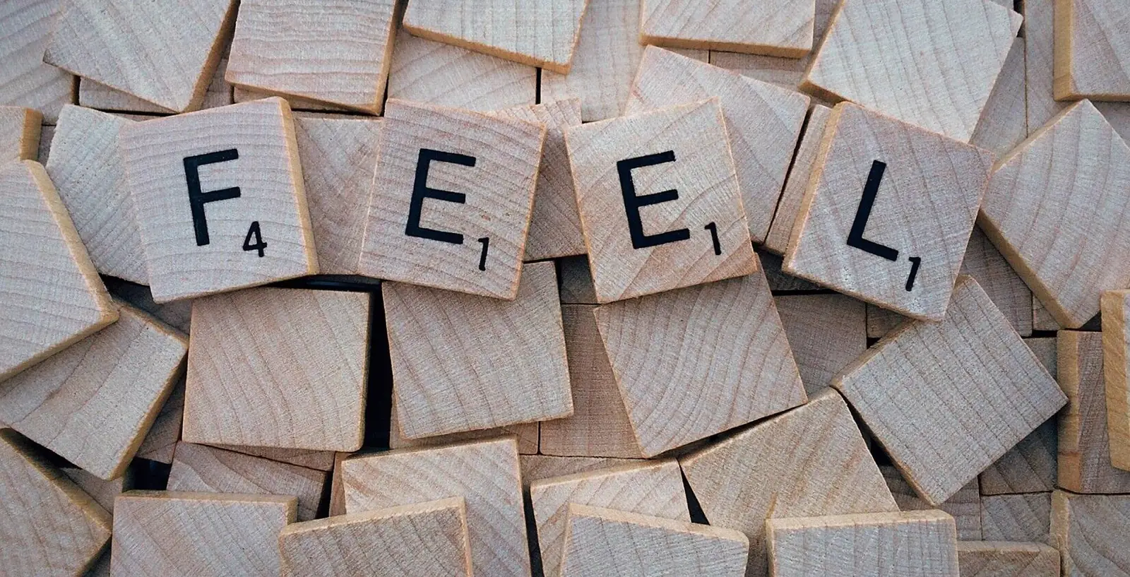 Fichas de madera con letras que forman la palabra FEEL, sobre un montón de fichas